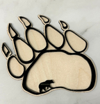 A laser-cut wooden bear paw print plaque with layered cutouts, shown on a light marble surface.