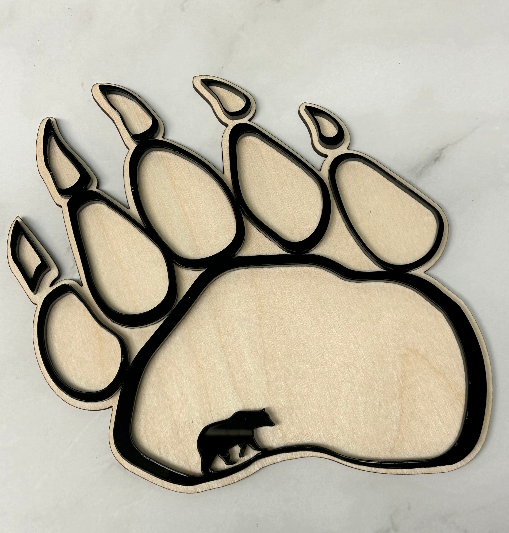 A laser-cut wooden bear paw print plaque with layered cutouts, shown on a light marble surface.