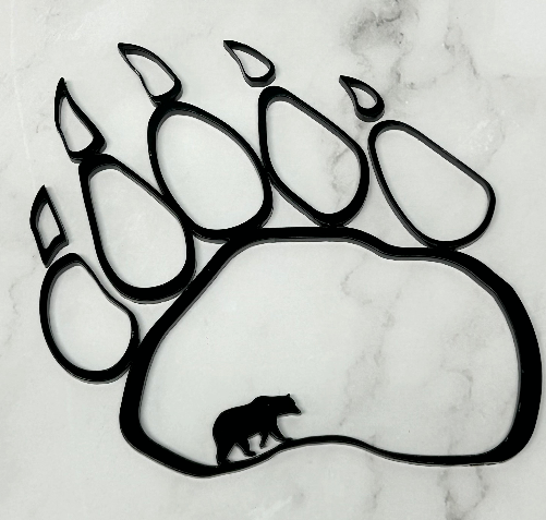A black bear paw print silhouette wall decor piece with a small bear silhouette inside the pad, displayed on a white marble surface.
