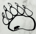 A black bear paw print silhouette wall decor piece with a small bear silhouette inside the pad, displayed on a white marble surface.
