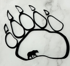 A black bear paw print silhouette wall decor piece with a small bear silhouette inside the pad, displayed on a white marble surface.